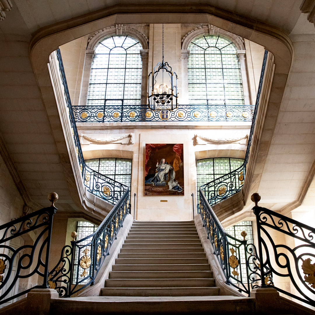 Main staircase at the Saint-Remi History Museum, with a painting by Hyacinthe Rigaud, “Louis XV in coronation robes”. ©Ville de Reims
